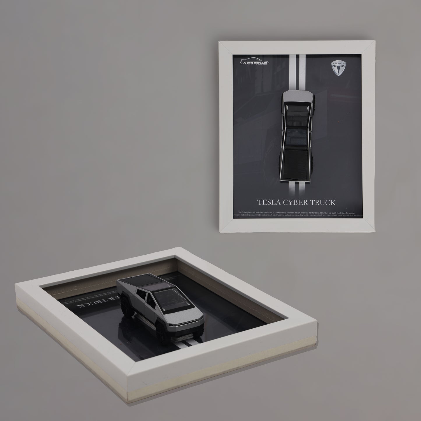 Framed model of a Tesla Cybertruck on a reflective surface with a matching framed poster on a gray wall.