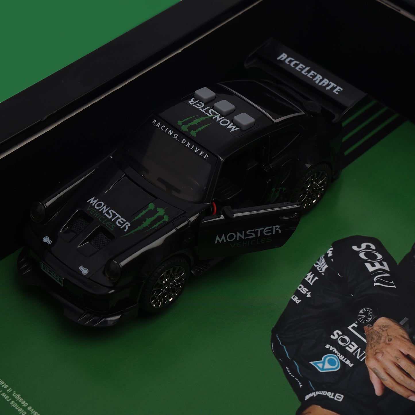 Toy car with 'Monster' branding on a green surface, next to a person wearing a racing glove.