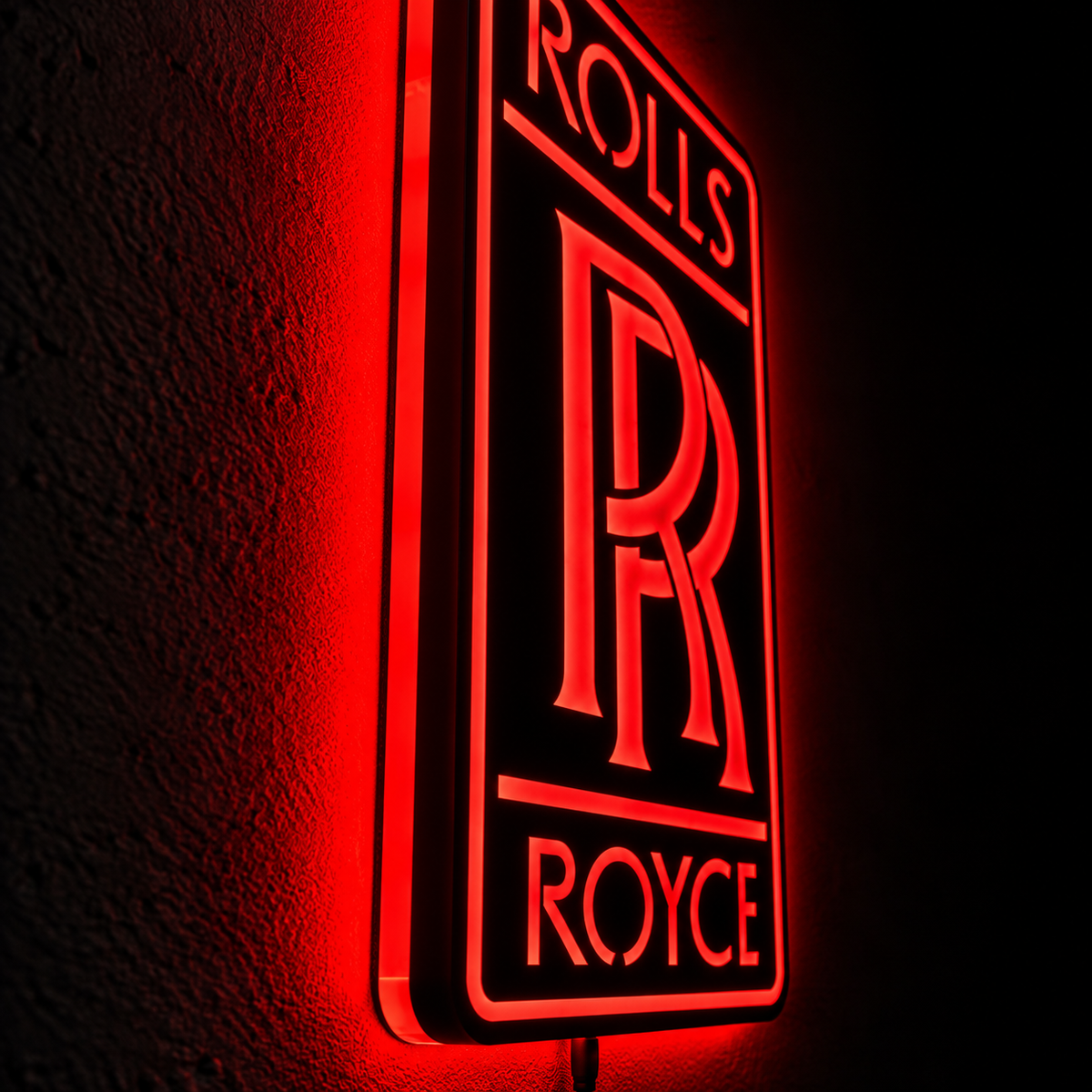 Rolls-Royce logo LED wall sign with golden illumination on a black rectangular plaque against a concrete wall
