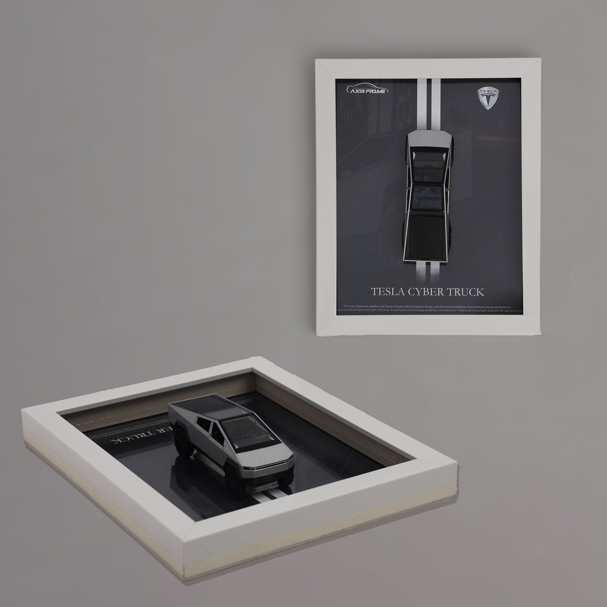 Framed model of a Tesla Cybertruck on a reflective surface with a matching framed poster on a gray wall.